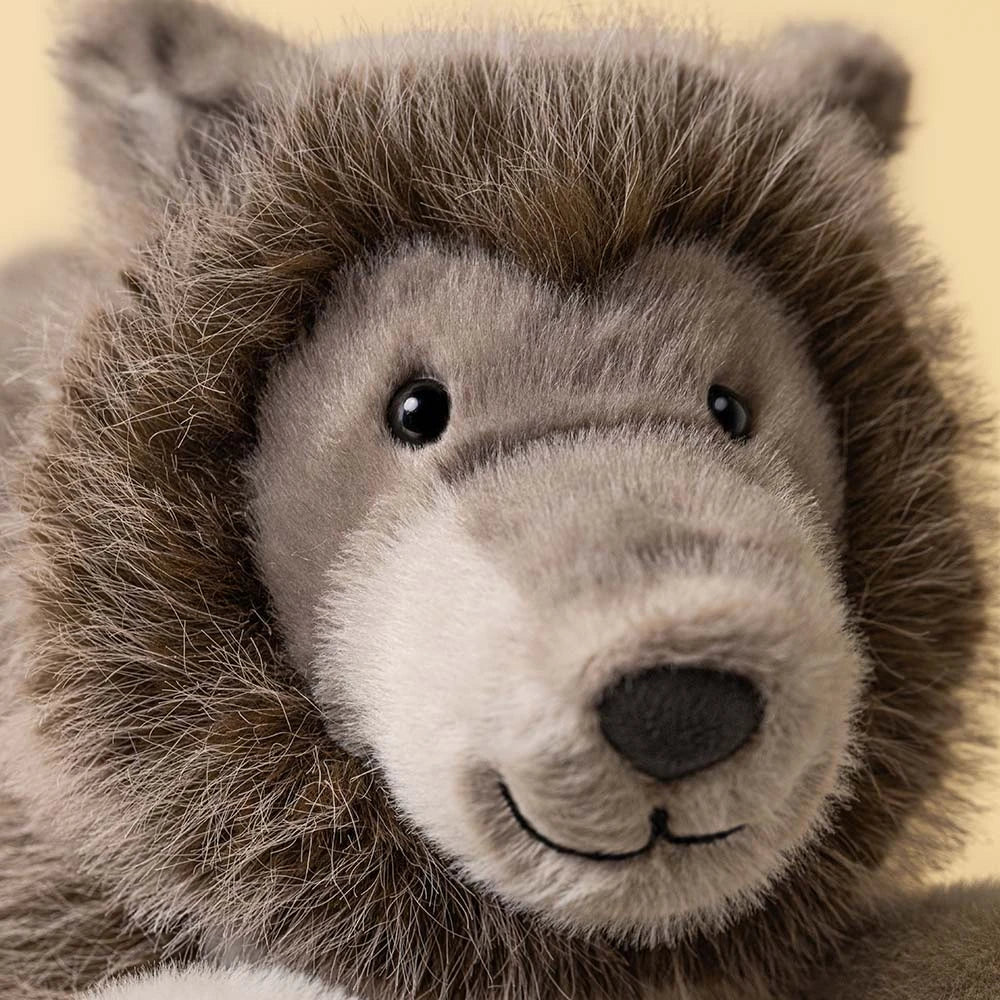 A plush stuffed animal shaped like a wolf lying down on a clean white background. The toy has a brown and gray body with a lighter beige muzzle and gray paws and legs.