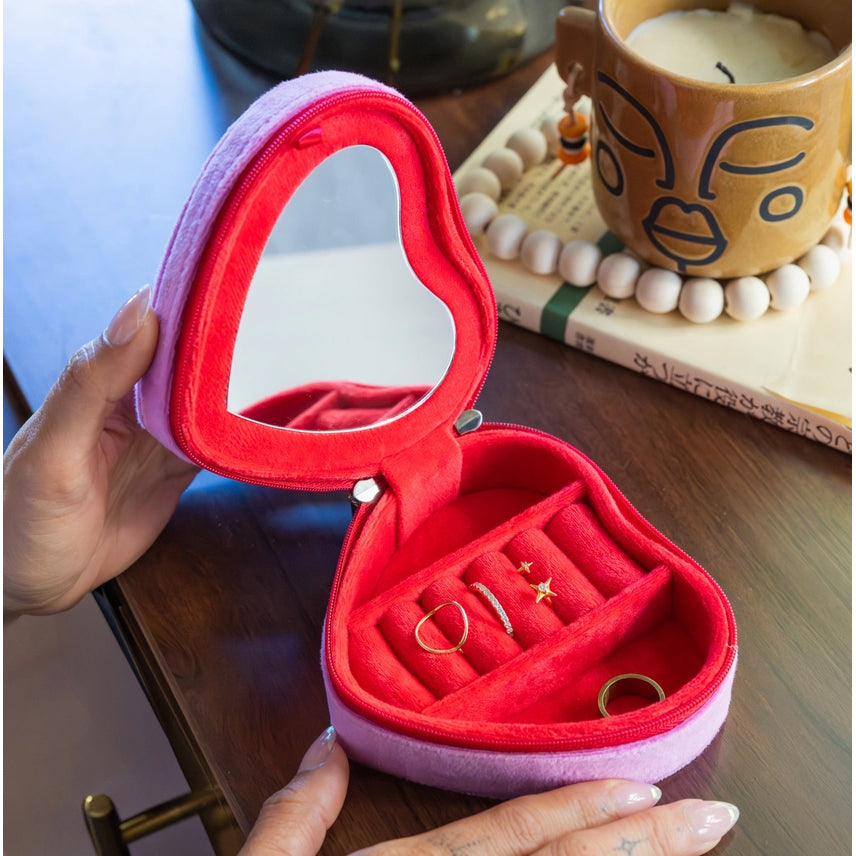 Heart-shaped jewelry box with rings on a wooden surface with a candle and books in the background.