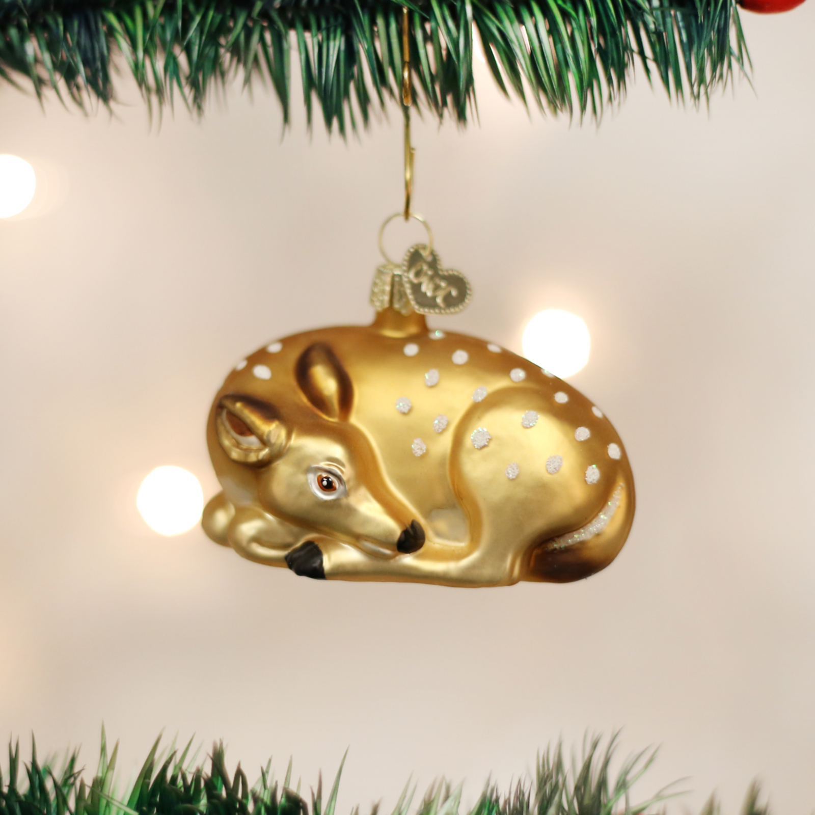 A gold-finished deer ornament shaped like a sleeping fawn, with white speckled spots, a small red eye, black nose, and a hanging loop at the top, shown on a plain white background.