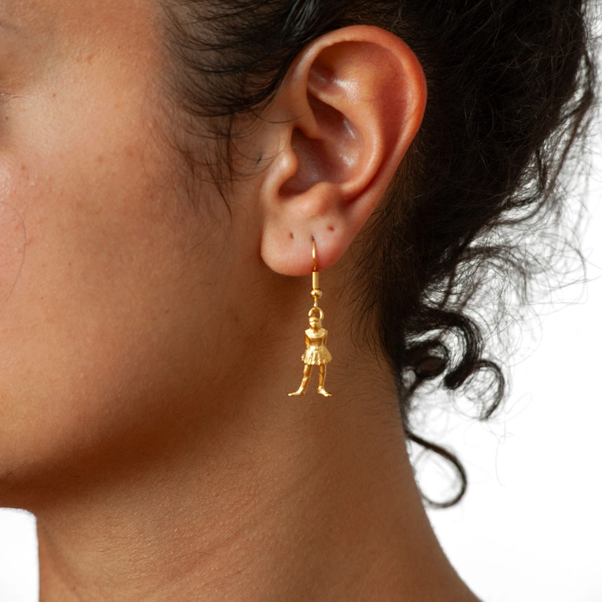 Close-up of a person wearing a gold earring with a small figure pendant.