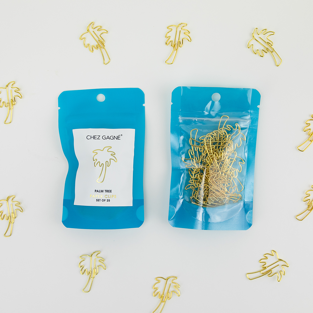 Two blue resealable pouches of gold paperclips arranged on a white background, surrounded by scattered gold palm tree decorations. One pouch has a white label reading 'CHEZ GAGNÉ' and 'PALM TREE' with 'SET OF 25'.