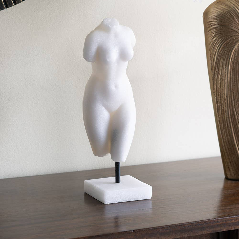 White marble sculpture of a torso on a wooden surface with decorative elements in the background.