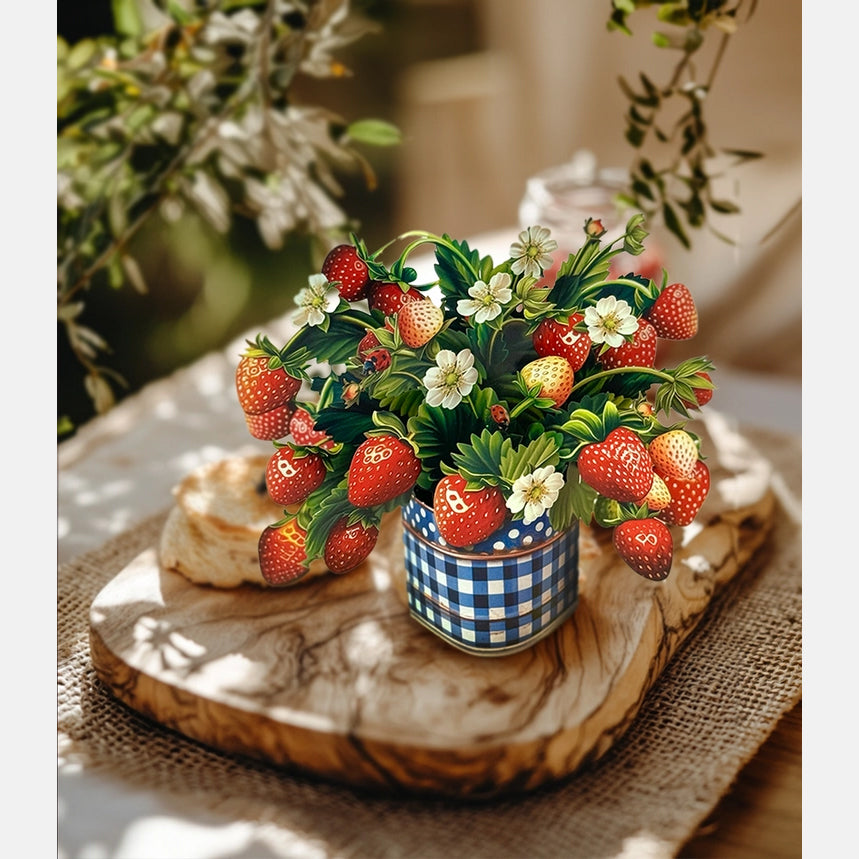 Decorative arrangement of strawberries and flowers in a checkered pot on a wooden board.