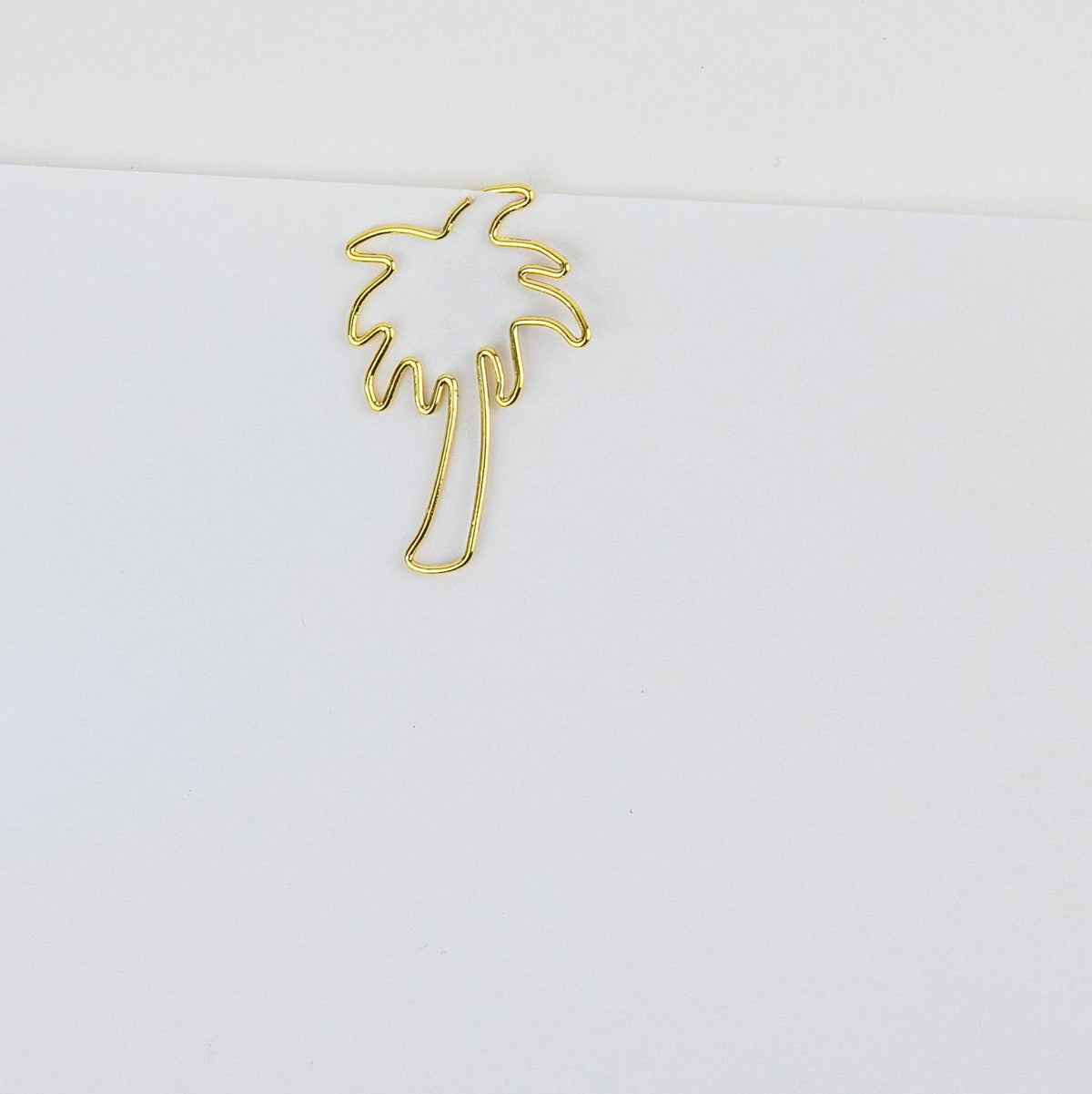 A small gold wire cutout of a palm tree, photographed on a plain white background.