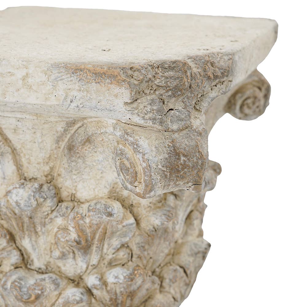 Close-up of an ornate carved stone or plaster decorative column capital with floral relief details and a rectangular top surface, shown against a plain white background.