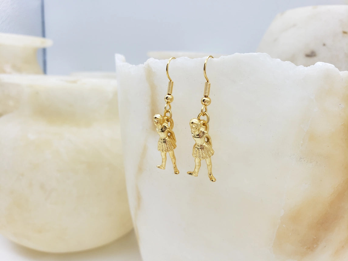 Gold ballerina shaped earrings on a white background