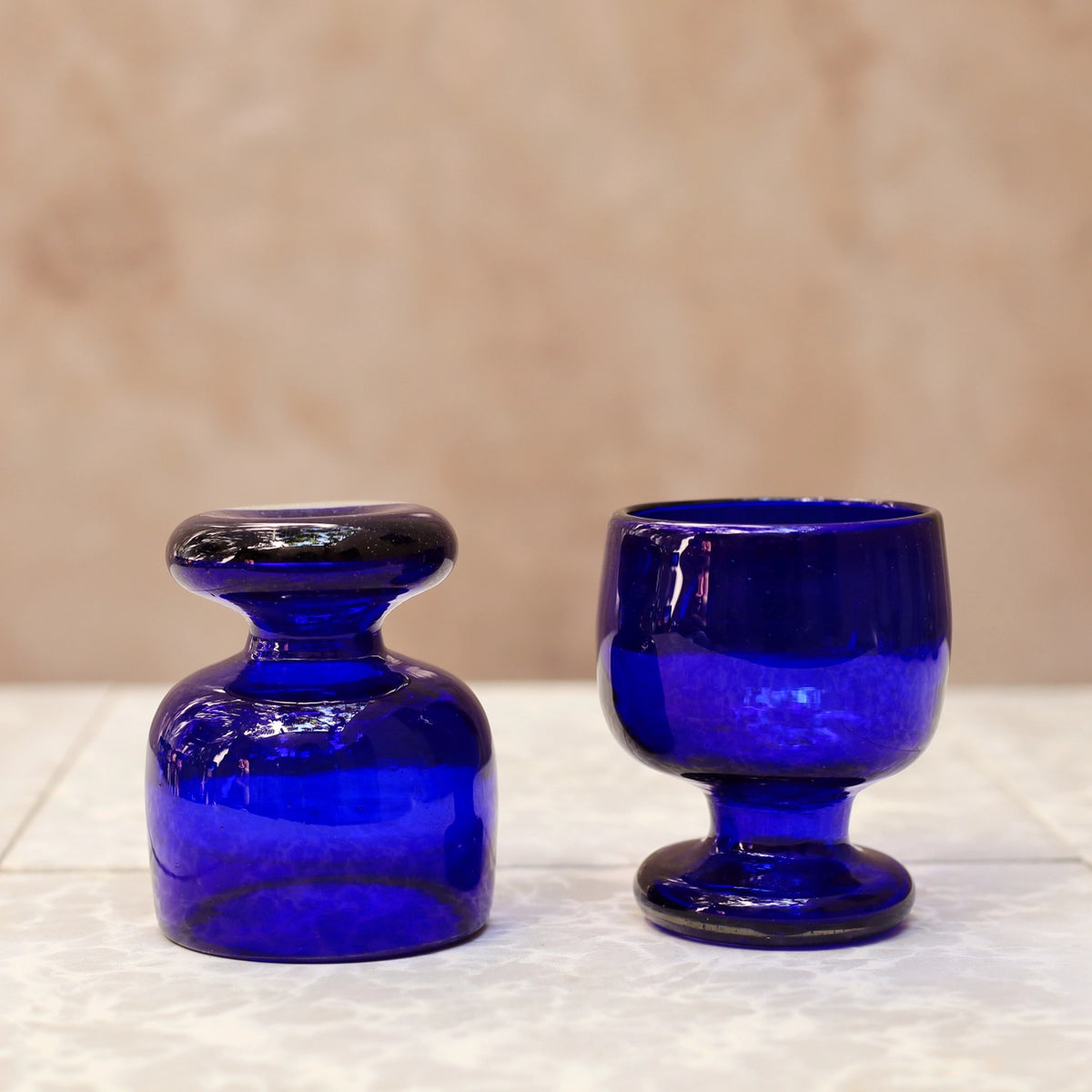 Two blue glass vessels on a textured surface with a beige background