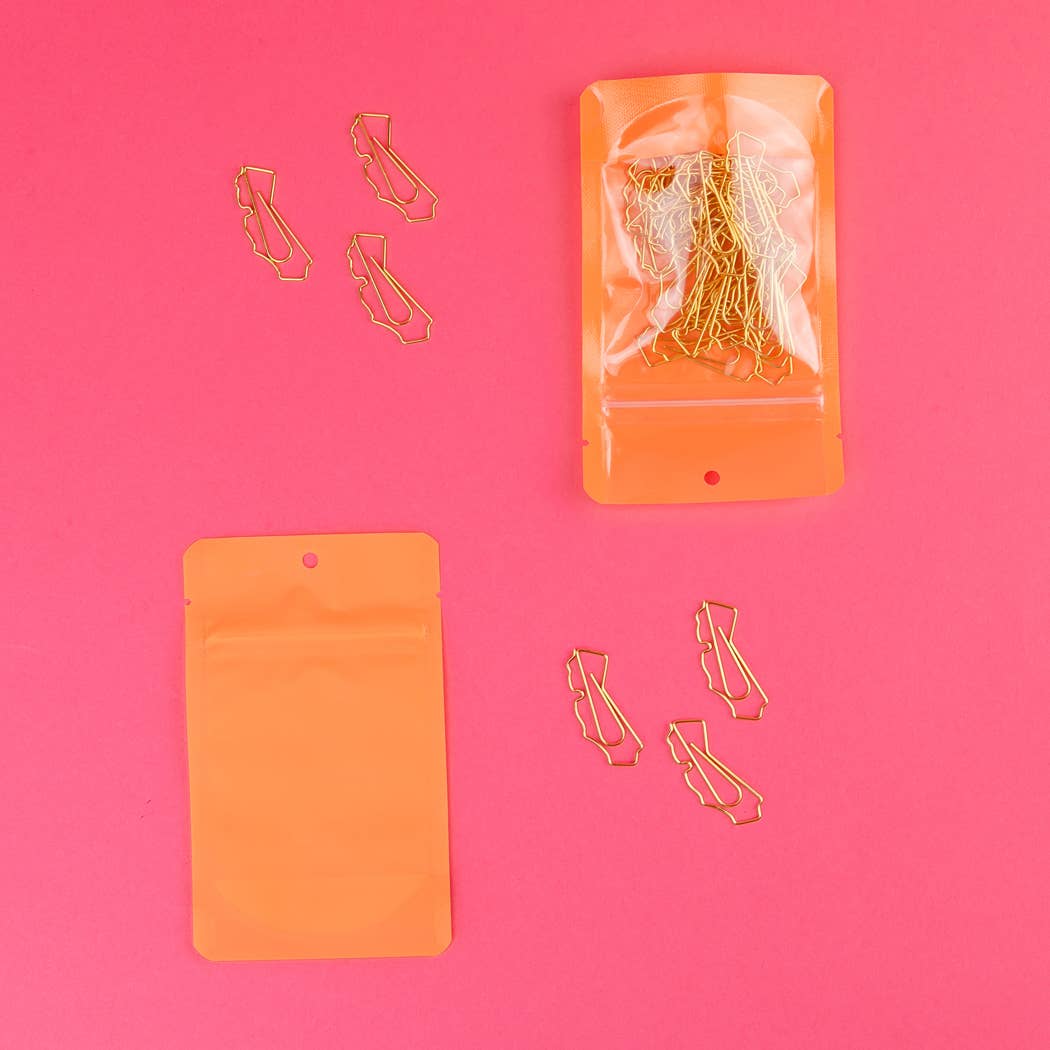 Gold paper clips on a pink background with orange packaging