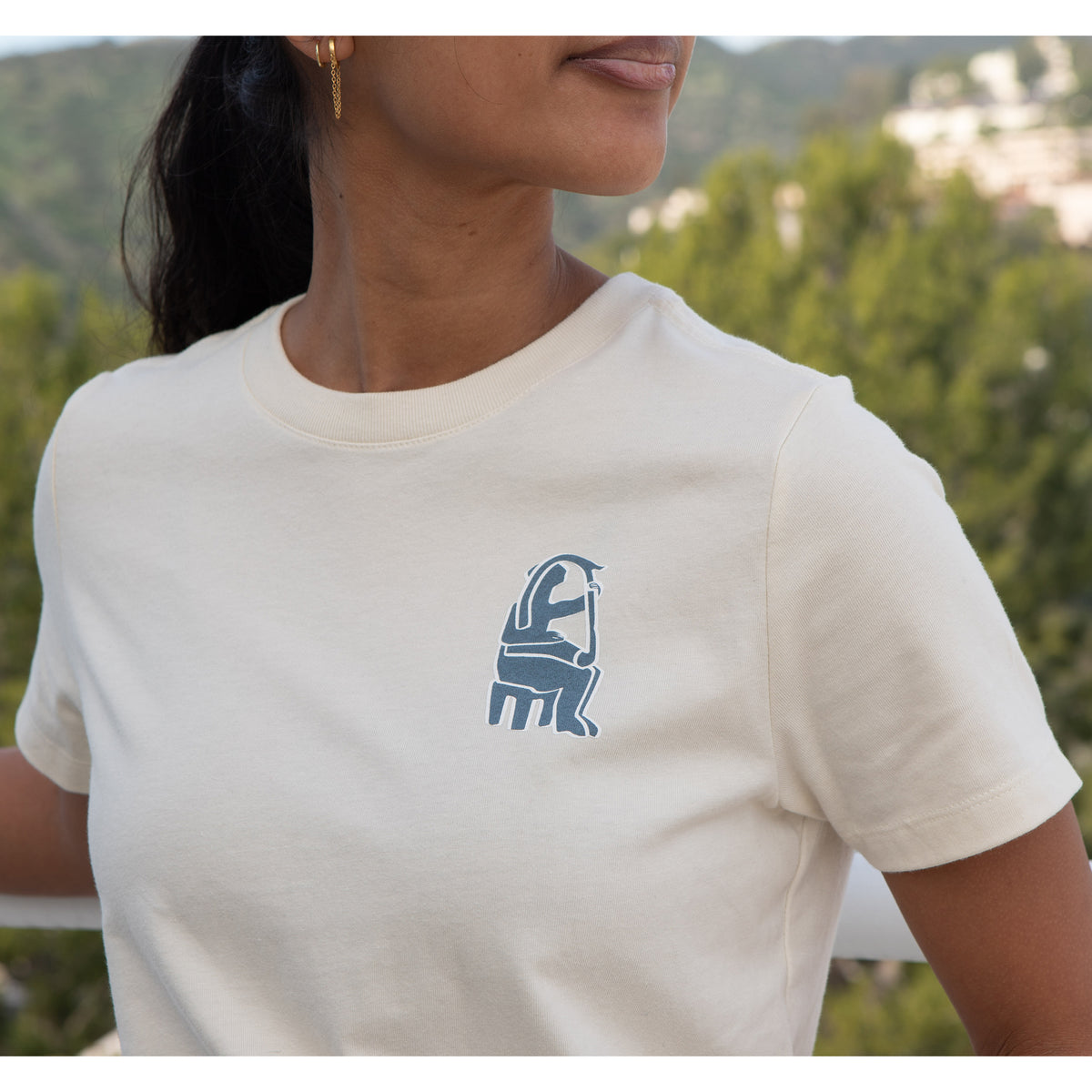 Person wearing a white t-shirt with a blue graphic design outdoors