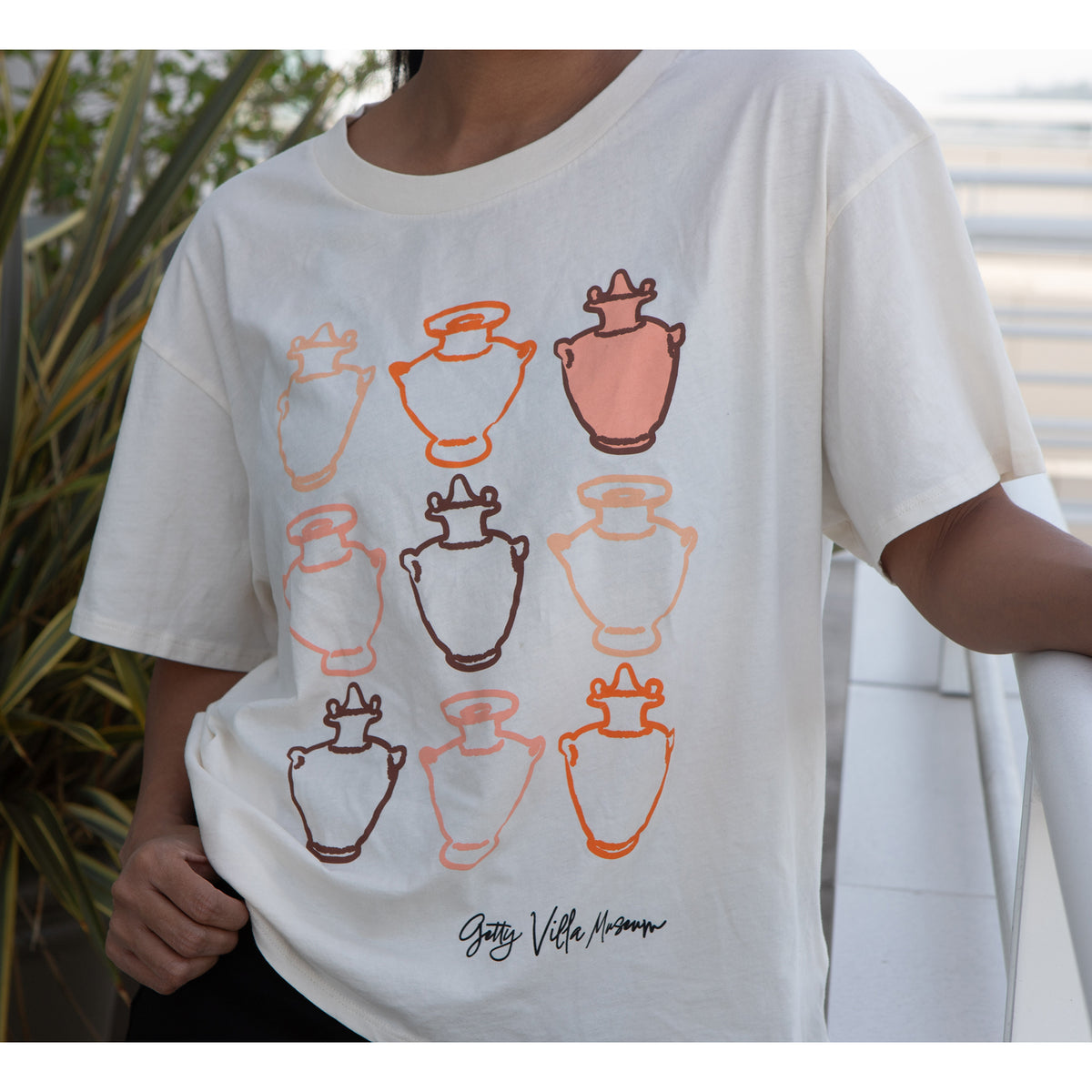 White t-shirt with graphic design of vases worn by a person outdoors.