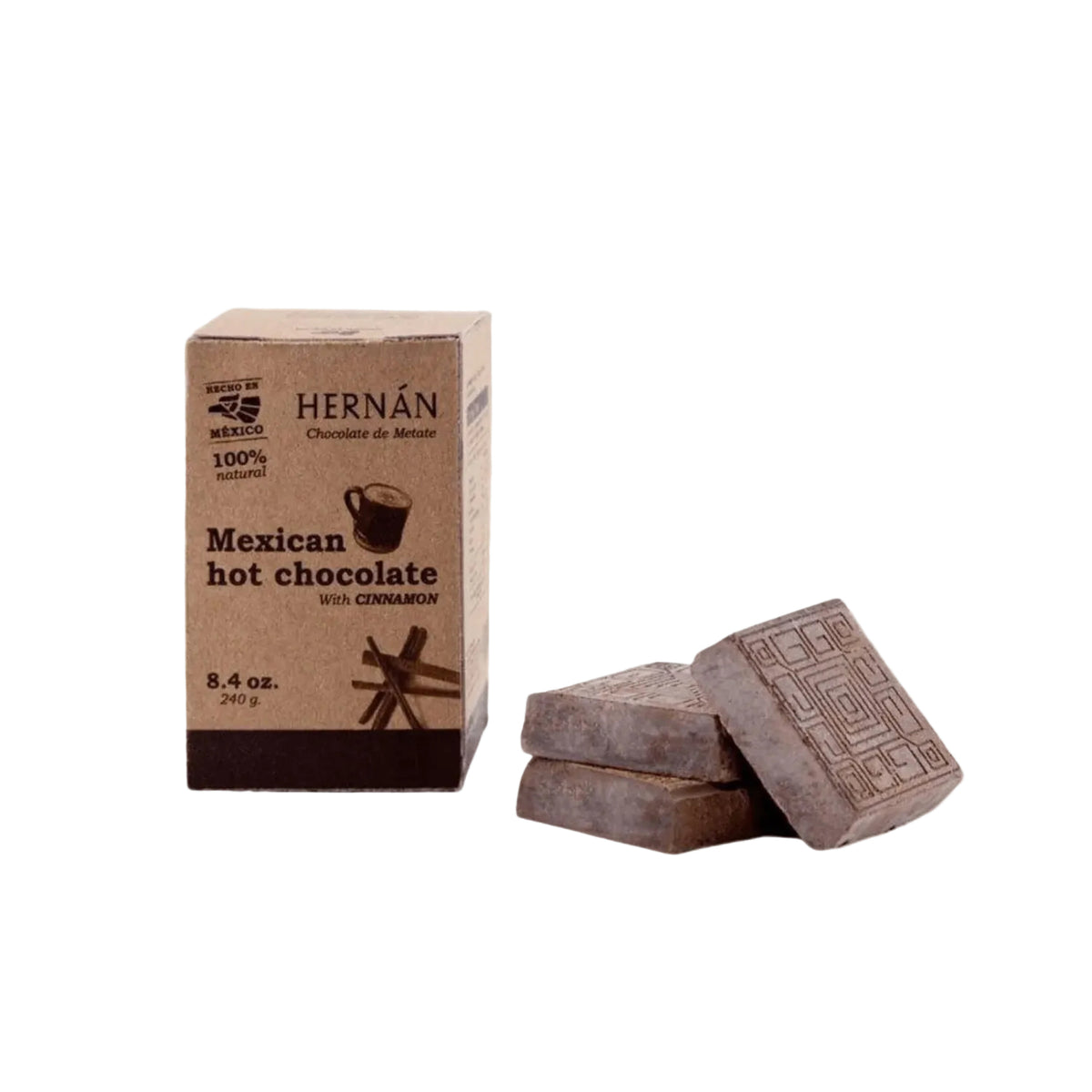 A box of Hernán Mexican hot chocolate with cinnamon next to two square chocolate pieces on a light beige background.