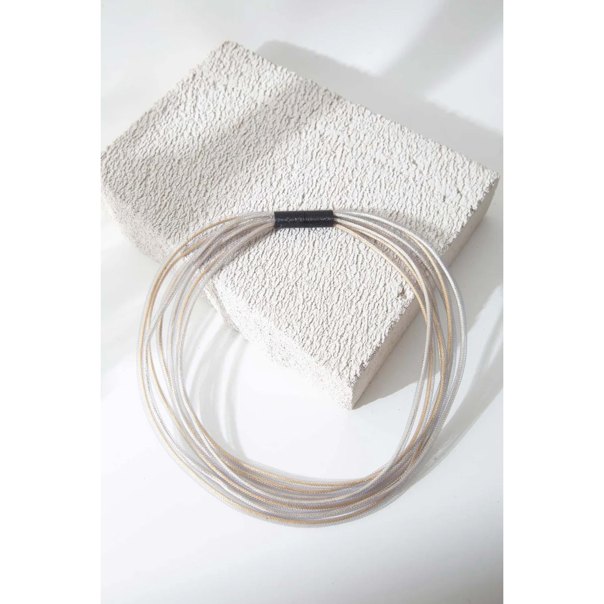 A set of thin, translucent beige cords coiled in a circle, held together by a small black band, displayed on a textured white stone block against a white background.