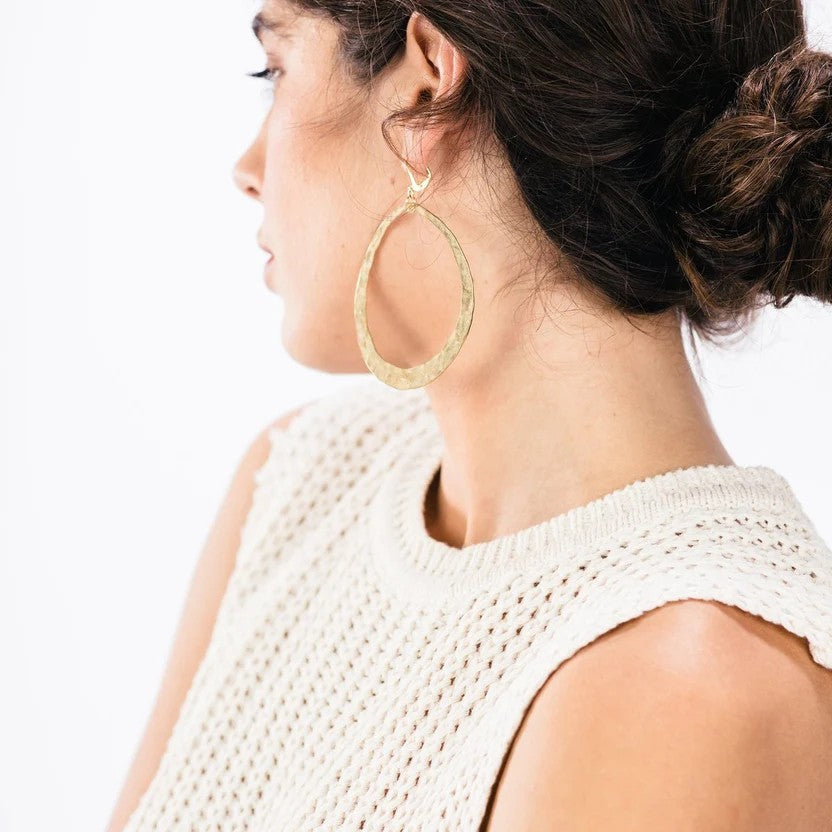 A pair of hammered gold-tone oval hoop earrings with fishhook backings, displayed against a solid white background.