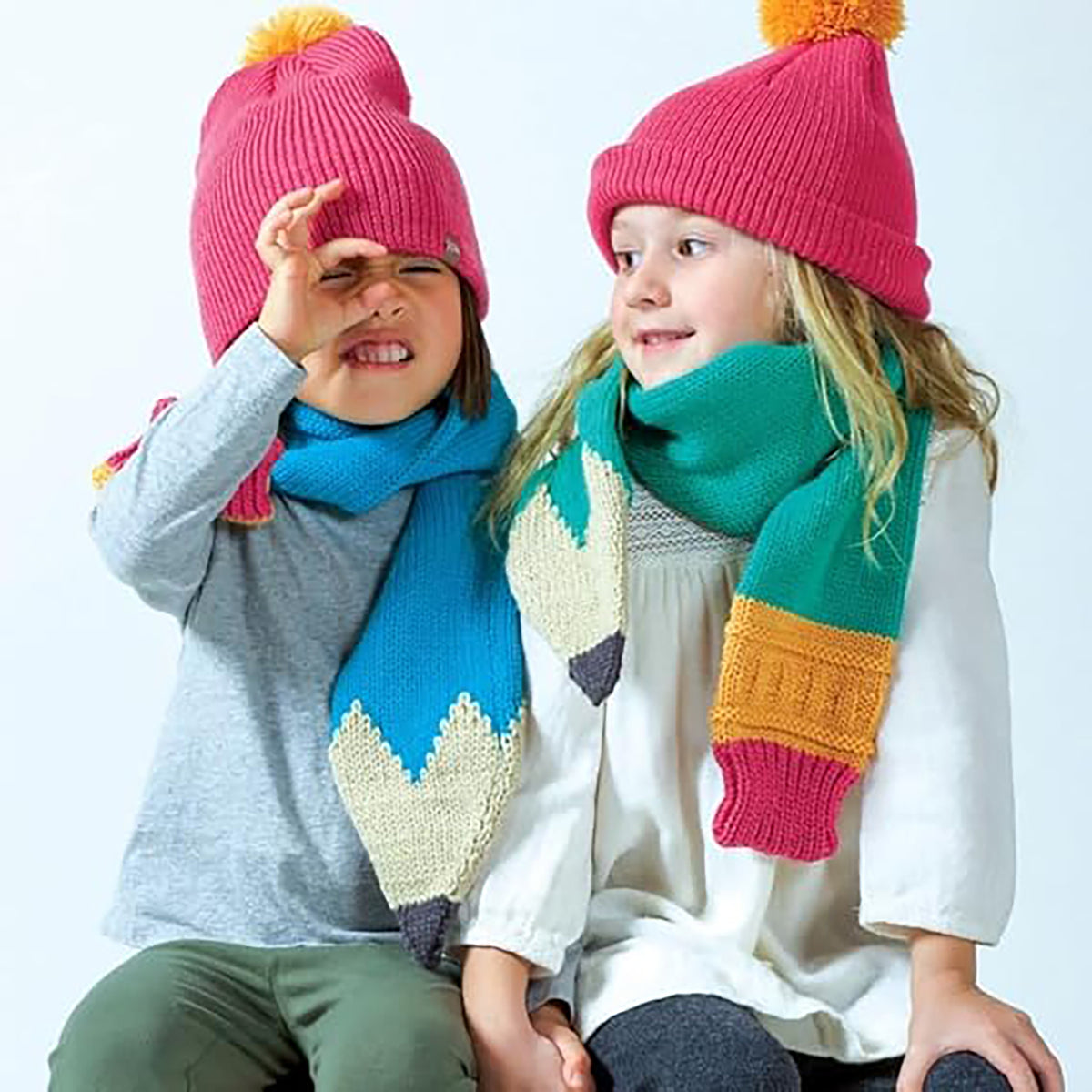 Two children wearing colorful knit hats and scarves on a white background