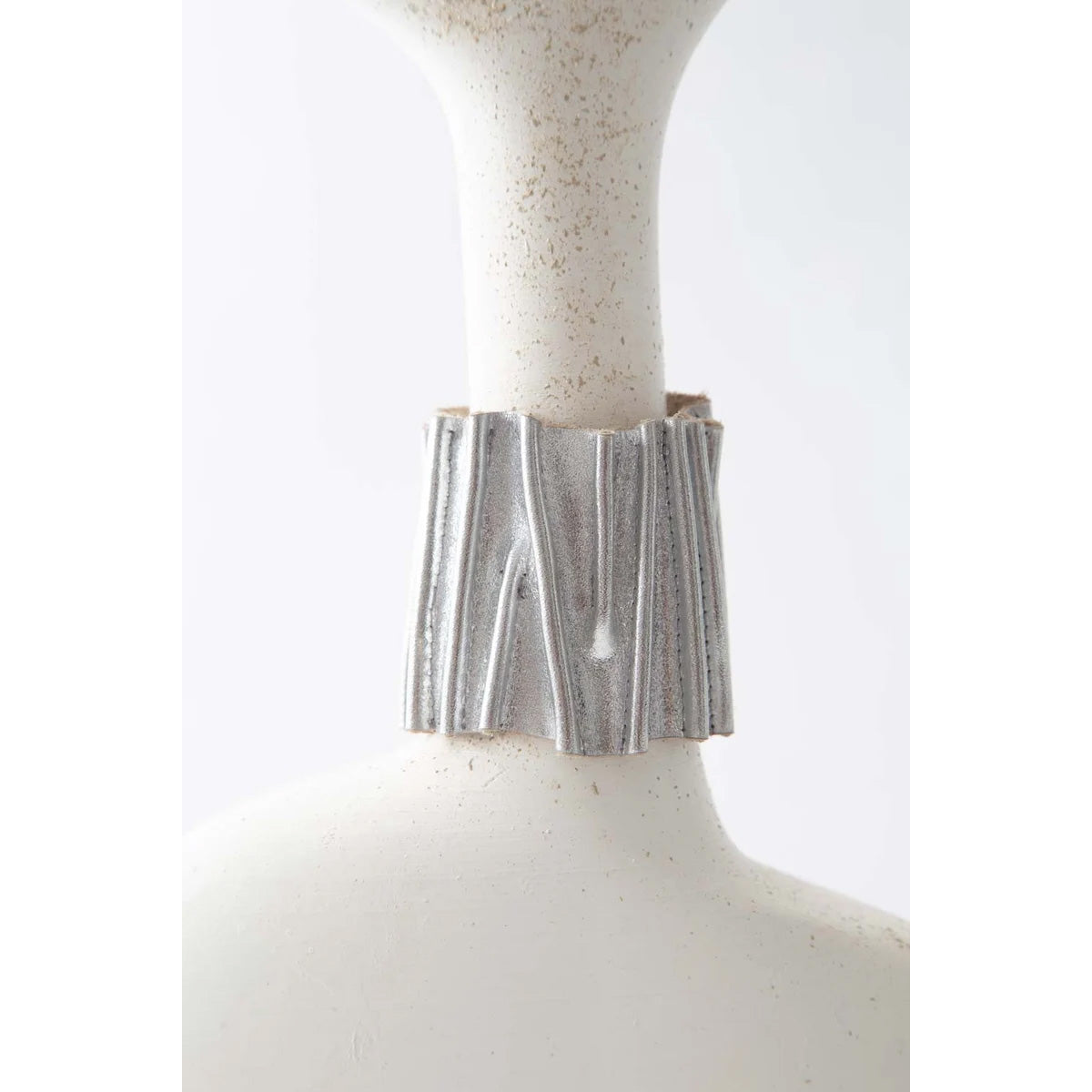 A wide silver metallic cuff bracelet with a textured, vertically fluted design, displayed on a white ceramic mannequin bust against a light gray background.