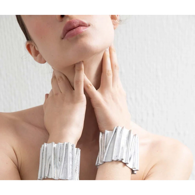 A wide silver metallic cuff bracelet with a textured, vertically fluted design, displayed on a white ceramic mannequin bust against a light gray background.