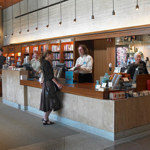 People interacting at a reception desk in a modern building with bookshelves in the background.