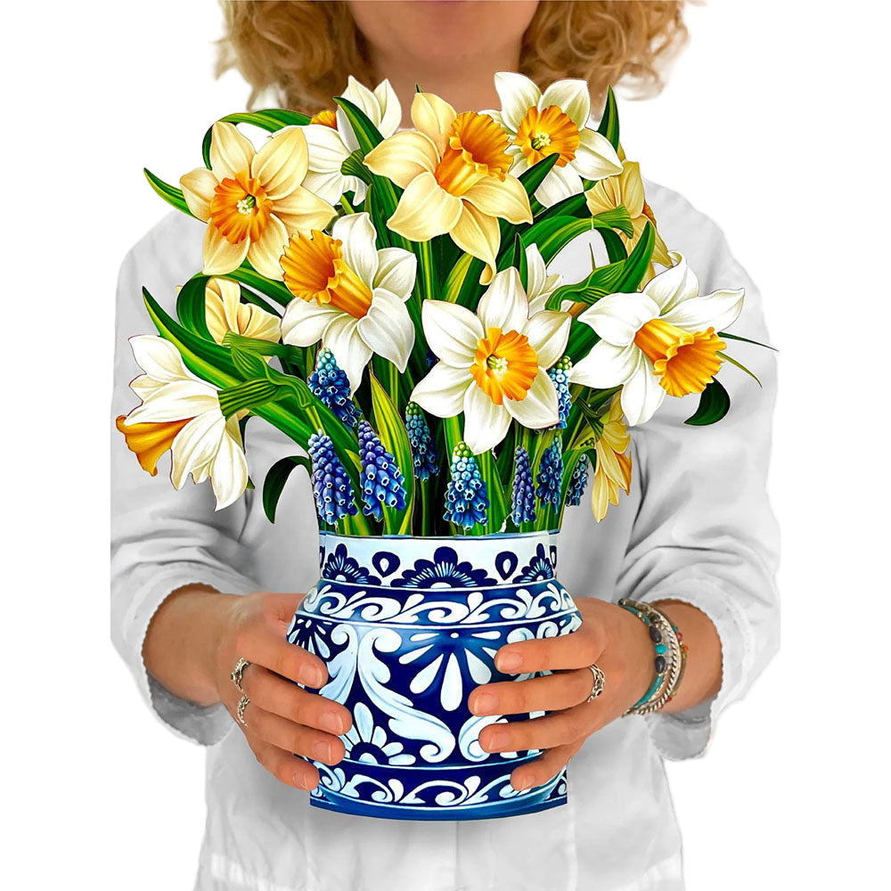Person holding paper daffodils in a blue and white paper vase
