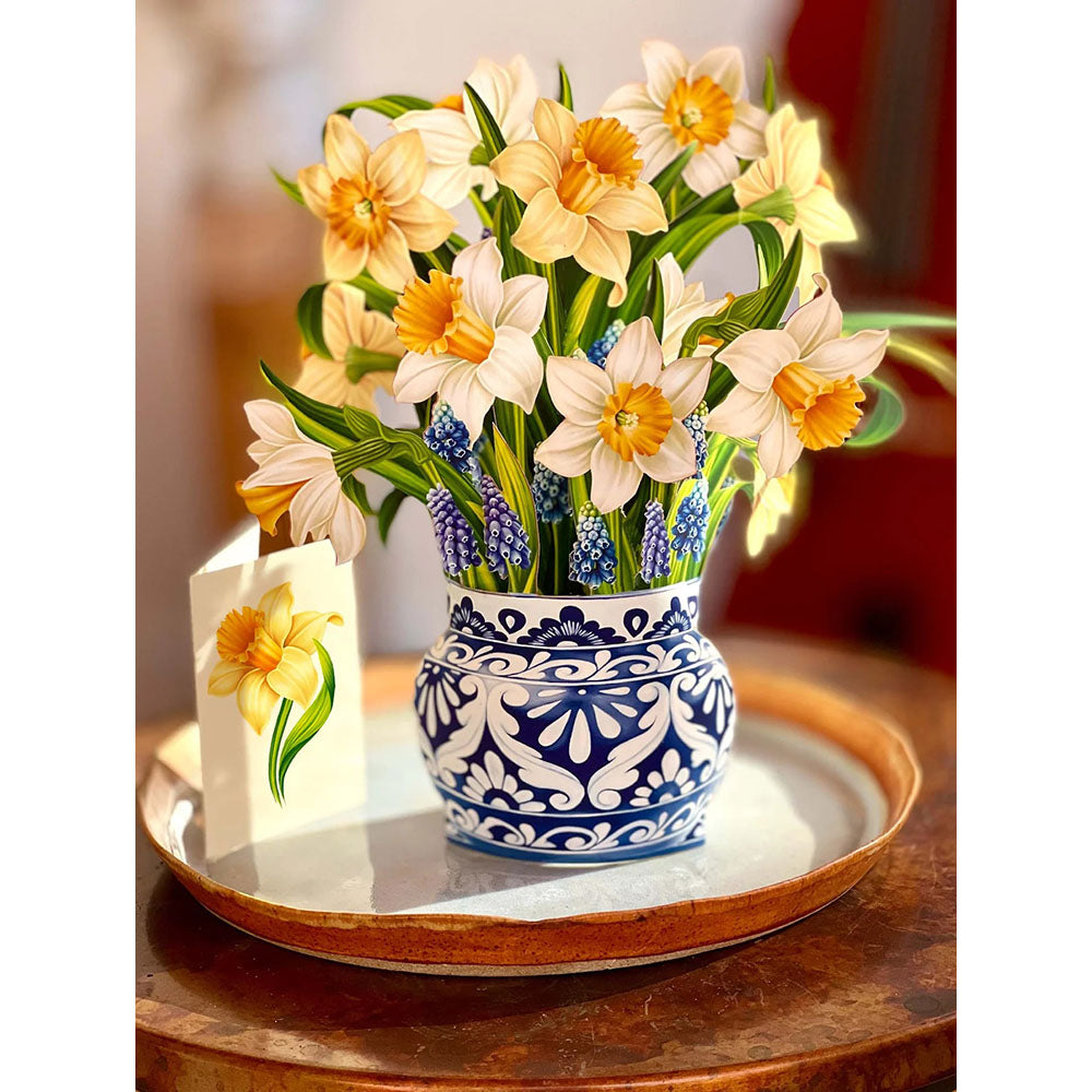 Person holding paper daffodils in a blue and white paper vase