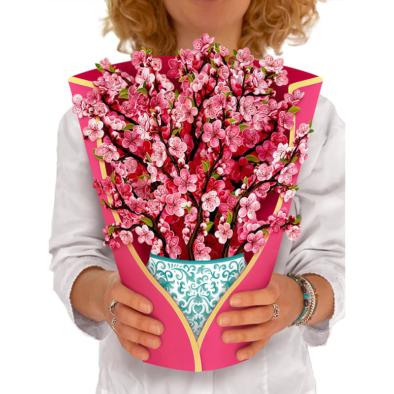 A bouquet of paper cherry blossoms in a blue and white patterned vase held by a woman
