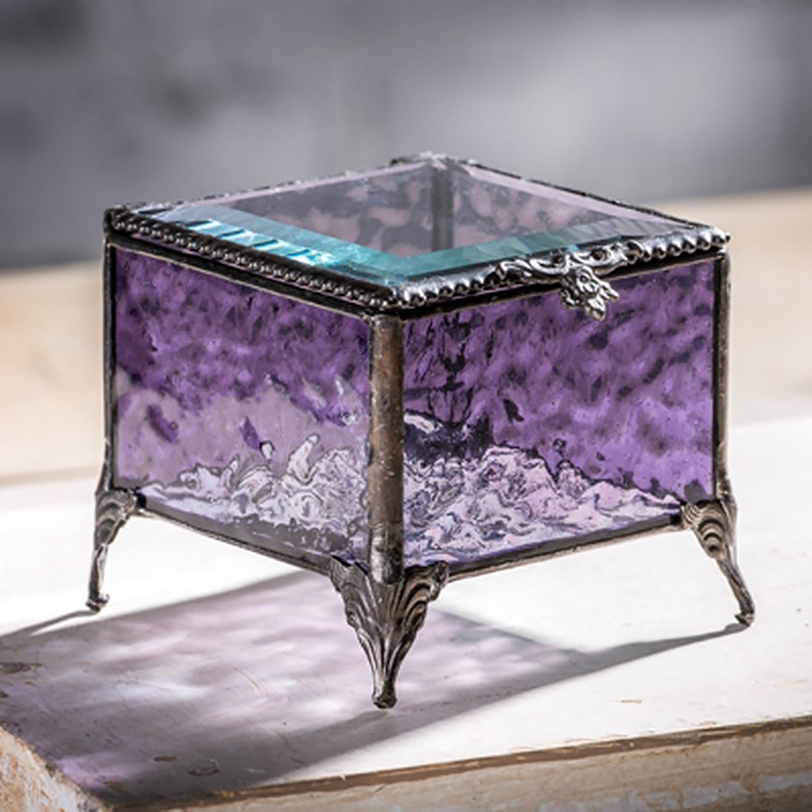 A vintage-style glass jewelry box with purple stained glass, metal trim, and decorative metal feet. 