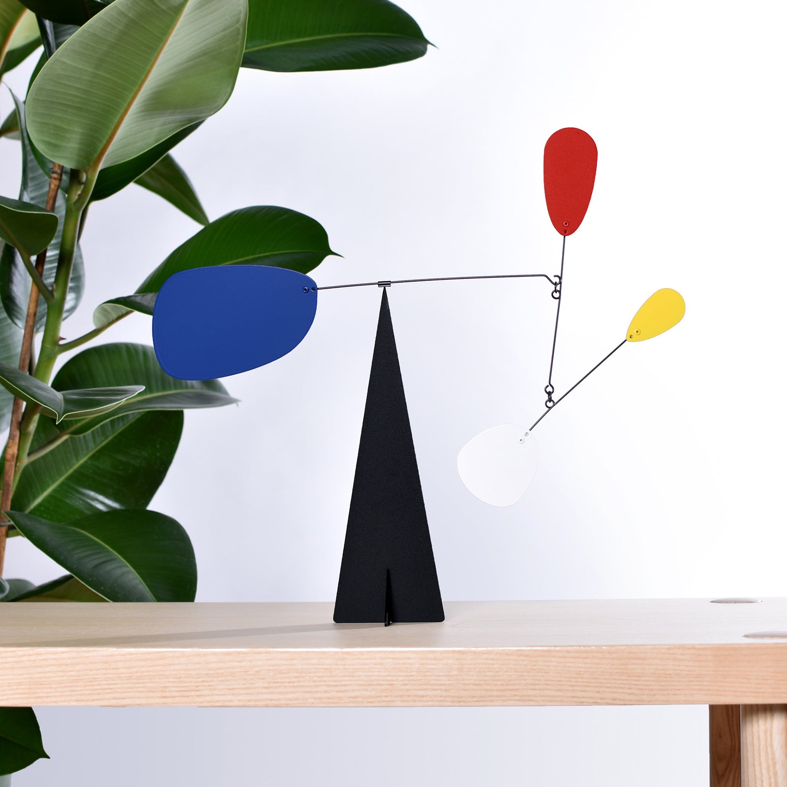 A contemporary metal desk mobile with elliptical shapes in blue, red, white, and yellow, balanced on a black stand.