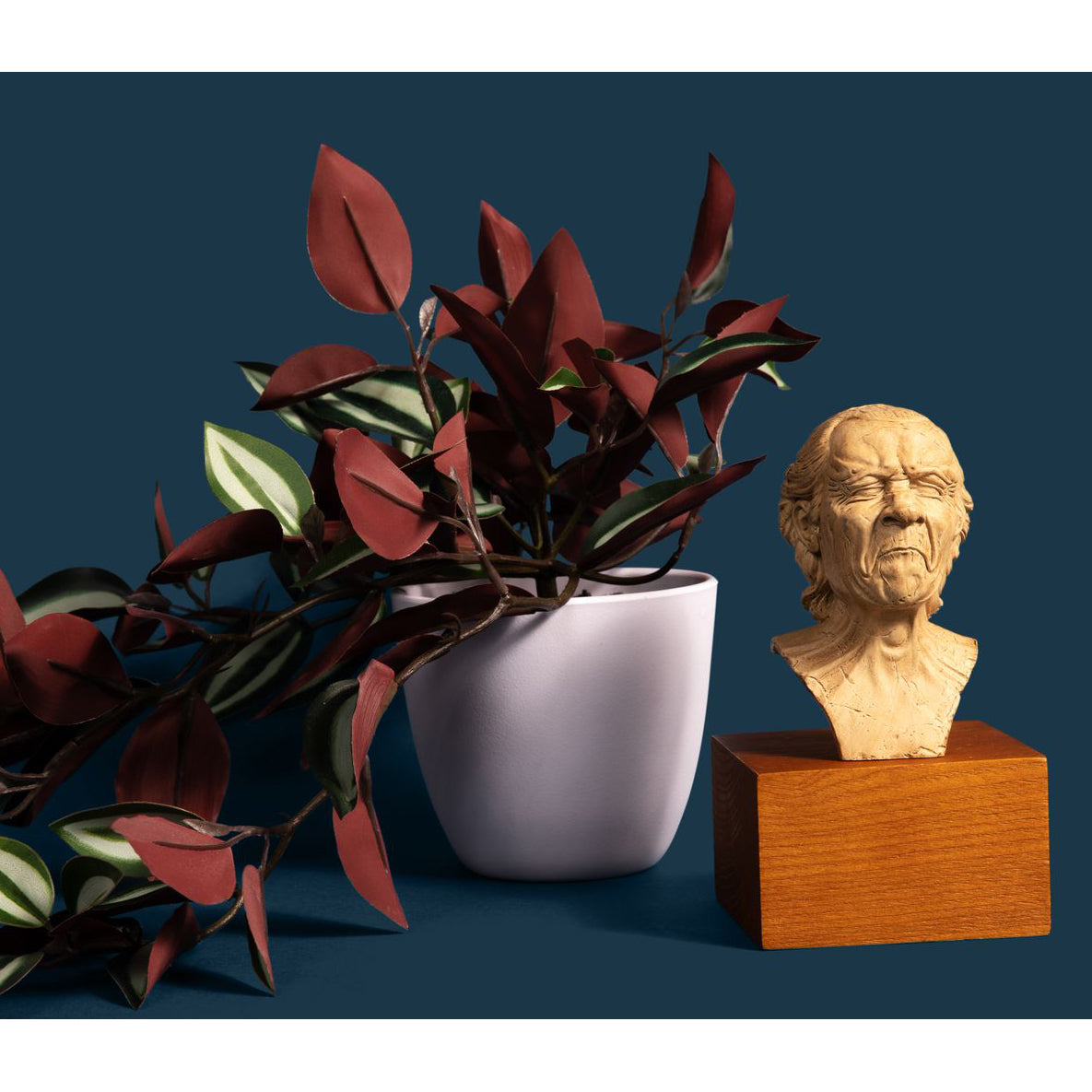 vexed man sculpture reproduction next to a potted plant in front of a blue background