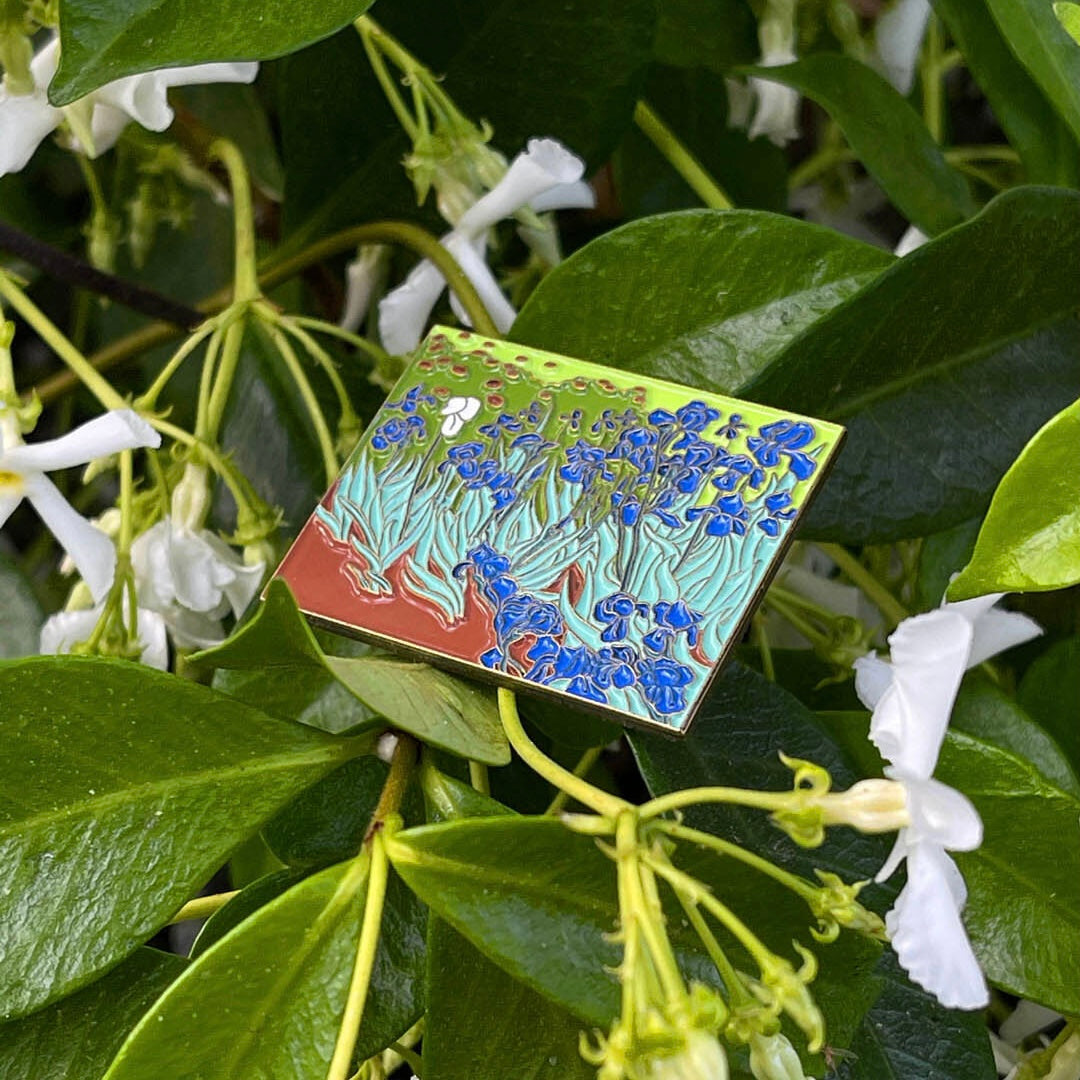 An enamel pin featuring a colorful floral design based on the 'Irises' painting by Vincent van Gogh.